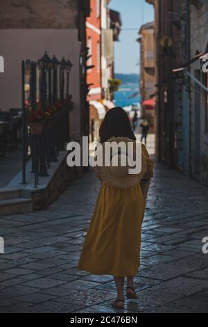 Junge hübsche Frau im gelben Kleid zu Fuß durch die kleinen Straßen der Stadt Porec Meer auf Hintergrund Stockfoto