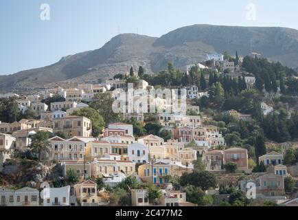 Schöne neoklassizistische Gebäude säumen die Bucht auf der charmanten griechischen Insel Symi. Eine dramatische Szene mit eleganten, bunten Häusern. Stockfoto