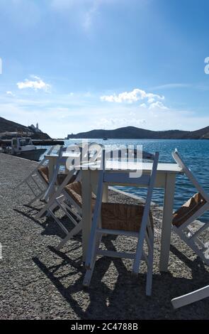 Traditionelle Taverna Tische und Stühle im Hafen der griechischen Ferieninsel iOS. Blick über die schöne Bucht des Hafens. Speicherplatz kopieren. Stockfoto