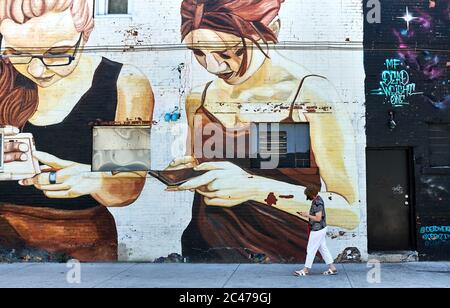 Frau benutzt Handy vor der Wandmalerei, die Frauen zeigt, die Handys benutzen. Leben imitiert Kunst. Kunst imitiert das Leben. Stockfoto