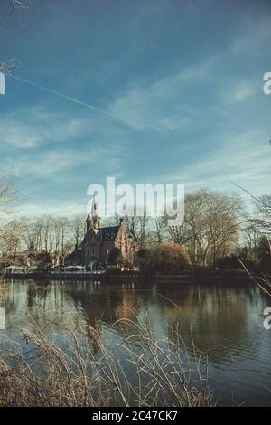 Vertikale Aufnahme einer alten Kirche am See umgeben Von blattlosen Bäumen Stockfoto