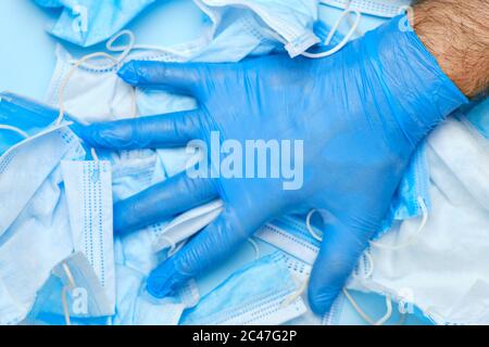 Mans Hand in Gummi blau Handschuh auf einem Hintergrund der verwendeten Schutzmaske Gesicht. Medizinischer Müll nach einer Coronavirus-Pandemie. Ende der Quarantäne. Stockfoto