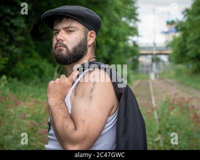 Junger, hübscher, bärtiger Mann mit Kohlestauben auf der Haut, der auf einer stillstehenden Eisenbahnstrecke mit Blumen mit natürlichem Licht in Par draußen aufgenommen wurde Stockfoto