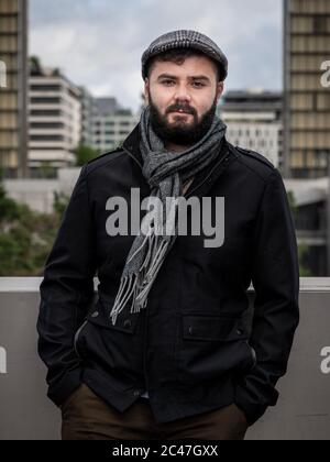 Junger hübscher französischer bärtiger Mann, draußen mit Gebäuden hinter dem Hotel mit natürlichem Licht in Paris, Frankreich, aufgenommen Stockfoto