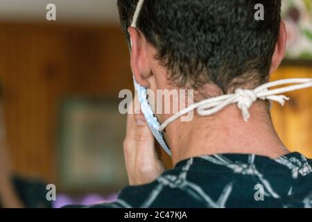 Junge männliche Anziehen Deluxe Stoff Maske Seite muskulösen jungen Mann in dunkel gemusterten Hemd auf hellem Holz Hintergrund Stockfoto