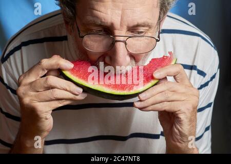 Nahaufnahme eines älteren Mannes mit Brille und gestreiftem Pullover, der ein Stück Wassermelone isst Stockfoto