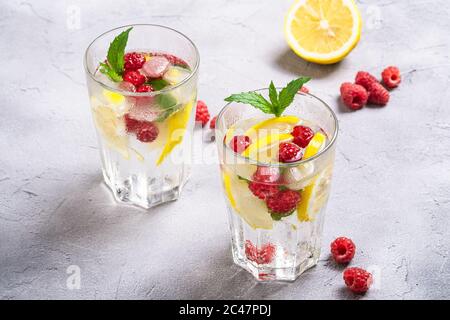 Frisches kaltes Eiswasser mit Zitrone, Himbeerfrüchten und Minzblatt in zwei facettierten Glas auf Steinbeton Hintergrund, Sommer Diät Getränk, Winkelansicht Stockfoto