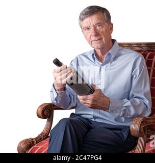 Freundlicher älterer Mann, der ein Etikett mit Weinflaschen untersucht, während er auf einem Stuhl sitzt und isoliert oder vor weißem Hintergrund ausspart Stockfoto