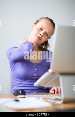 Arbeiten zu hart - junge Frau auf einem Computer in einem Büro arbeiten, Rückenschmerzen, Überlastung mit Arbeit, zu viel sitzen, setzen zuviel st Stockfoto