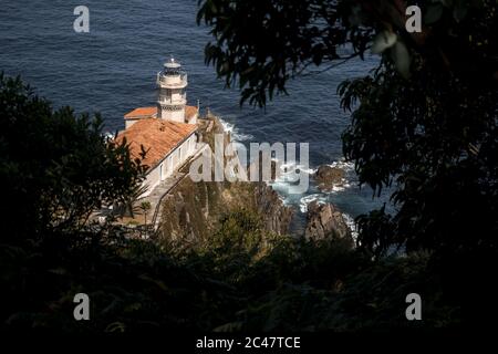 High-Angle-Aufnahme des Leuchtturms entlang des Meeres und Unter grünen Bäumen in Spanien gefangen Stockfoto