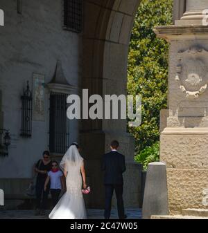 Rückansicht von Braut und Bräutigam, die in den Säulengang in Richtung Innenhof und versunkenen Garten des Santa Barbara County Courthouse, CA, gehen Stockfoto