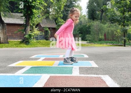 Kleines Mädchen in einem rosa Kleid spielen hopscotch auf Spielplatz im Freien, Kinder Aktivitäten im Freien Stockfoto