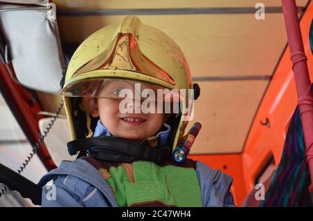 Kleiner Junge, der wie ein Feuerwehrmann agiert. Junge sitzt in einem echten Feuerwehrauto Stockfoto