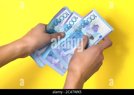 Zehntausend Tenge in den Händen der Frauen. Gelber Hintergrund. Stockfoto