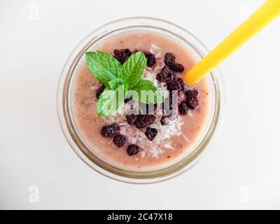 Frischer, selbstgemachter Pink Smoothie mit getrockneten Heidelbeeren, Kokosnuss- und Minzblättern auf der Oberseite. Gesunde Ernährung mit Früchten. Auf hellem Hintergrund. Stockfoto