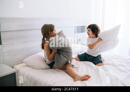 Zwei Brüder, 7 und 4 Jahre alt, blond und braun kaukasisch, spielerisch kämpfen im Bett mit weißen Laken mit grauen und weißen Kissen Stockfoto