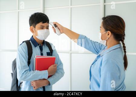 Asiatische Frau Lehrer mit Thermometer Temperatur Screening Schüler für Fieber gegen die Ausbreitung von COVID-19, während Schüler wieder in die Schule, Neu Stockfoto