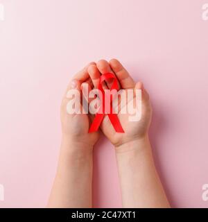 Konzept für Gesundheit und Medizin - Kinder Hände halten rotes AIDS-Sensibilisierungsband auf rosa, Banner für National Blood Donor Month im Januar, World AIDS d Stockfoto