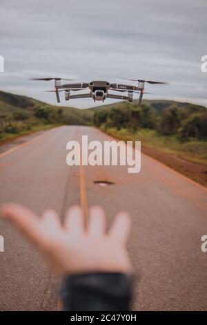 Vertikales Bild einer Drohne, die im über die Straße fliegt Landschaft mit einer verschwommenen Hand im Vordergrund Stockfoto
