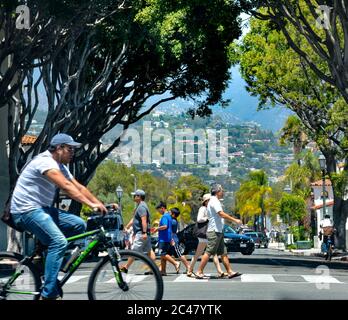 Weit entfernte Residenzen in den Ausläufern, mit Fußgängern und Radfahrern in der Kreuzung der State Street in der Innenstadt von Santa Barbara, CA Stockfoto
