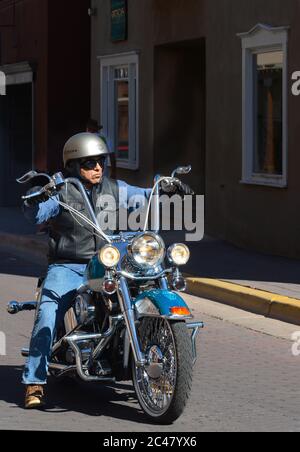 Ein Mann, der ein kundenspezifisches Harley-Davidson Motorrad mit Affe-Hanger-Lenker reitet, fährt entlang einer Straße in Santa Fe, New Mexico. Stockfoto