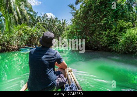 Ein Mann auf einem Bambusfloß rast einen Fluss durch einen fabelhaften grünen Dschungel hinunter. Reise nach Thailand. Stockfoto