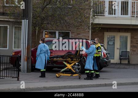 Die Bahre wurde von Sanitätern mit persönlicher Schutzausrüstung und medizinischen Kleidern aus dem Krankenwagen genommen. Medizinische Liege bereit, kranke Patienten zu transportieren. Stockfoto