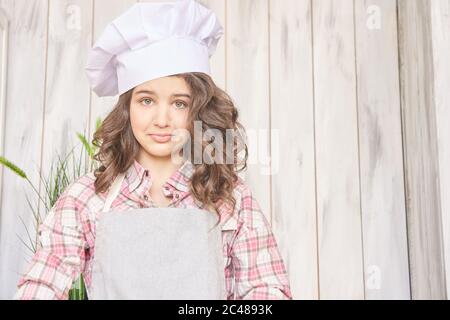 Schönes Mädchen. Kleiner hübscher Koch-Meister. Weiße Kappe. Braune lockige Haare Stockfoto