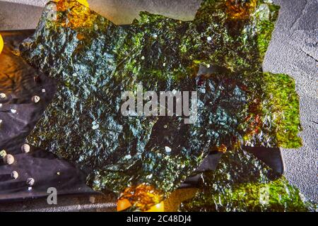 Knusprige Nori-Algen mit Kirschtomaten und dunklen Gewürzen auf grauem Beton. Japanisches Essen Nori. Getrocknete Blätter von Algen. Nahaufnahme Stockfoto