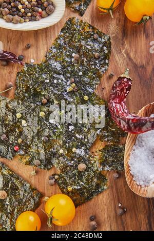 Knusprige Nori-Algen mit Kirschtomaten und Gewürzen auf einem Holzbrett. Japanisches Essen Nori. Getrocknete Blätter von Algen. Flach liegend Stockfoto