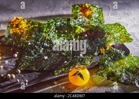 Knusprige Nori-Algen mit Kirschtomaten und dunklen Gewürzen auf grauem Beton. Japanisches Essen Nori. Getrocknete Blätter von Algen. Speicherplatz kopieren. Stockfoto