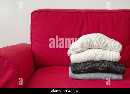 Nahaufnahme der warmen Pullover auf dem roten Sofa im Wohnzimmer Stockfoto