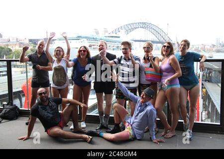 Einige Leute auf der Sydney No Pants Subway Fahrt warten auf dem Bahnsteig am Circular Quay Bahnhof mit der Sydney Harbour Bridge im Hintergrund. Stockfoto