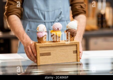 Verkäufer setzt einen Stand mit drei leckeren Eis in Waffelkegel mit verschiedenen Geschmack auf der Theke eines Geschäfts, close-up Stockfoto