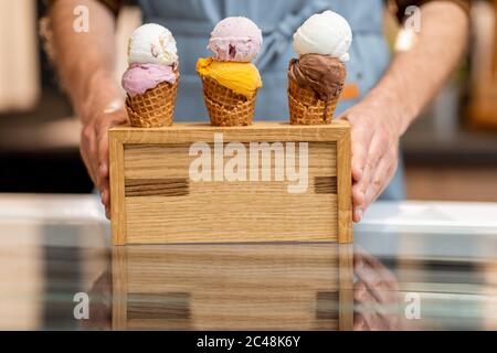 Verkäufer setzt einen Stand mit drei leckeren Eis in Waffelkegel mit verschiedenen Geschmack auf der Theke eines Geschäfts, close-up Stockfoto