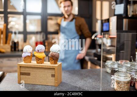 Leckeres Eis in Waffelkegel mit unterschiedlichem Geschmack auf der Theke eines Shops mit Verkäufer im Hintergrund Stockfoto