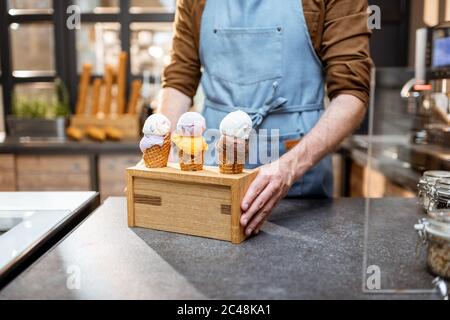 Verkäufer setzt einen Stand mit drei leckeren Eis in Waffelkegel mit verschiedenen Geschmack auf der Theke eines Geschäfts, close-up Stockfoto