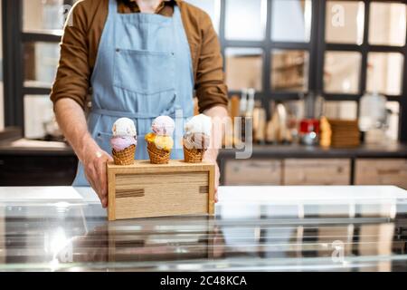 Verkäufer setzt einen Stand mit drei leckeren Eis in Waffelkegel mit verschiedenen Geschmack auf der Theke eines Geschäfts, close-up Stockfoto