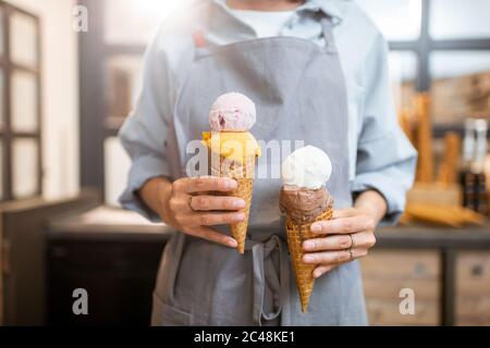 Verkäuferin hält zwei leckere Eiscreme im Waffelkegel im Laden, Nahaufnahme Stockfoto
