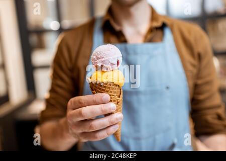 Verkäufer in Schürze hält Eis in einem Waffelkegel, Nahaufnahme. Verkauf von Eis in einem Geschäft Stockfoto