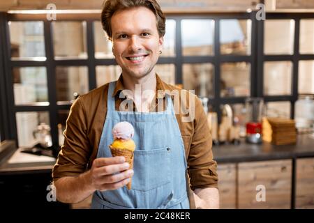 Portrait eines fröhlichen Eisverkäufer in Arbeitsuniform hält Eis in Waffelkegel im Shop Stockfoto