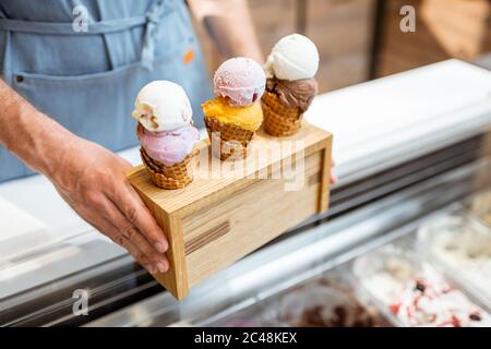 Verkäufer setzt einen Stand mit drei leckeren Eis in Waffelkegel mit verschiedenen Geschmack auf der Theke eines Geschäfts, close-up Stockfoto