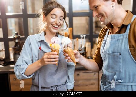 Zwei Verkäufer jubeln mit leckeren Eiscreme im Waffelkegel, haben Spaß beim Verkauf von Eis im Laden Stockfoto
