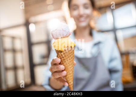 Weibliche fröhliche Verkäuferin hält leckere Eis in Waffelkegel drinnen, Verkauf von Süßigkeiten im Shop Stockfoto