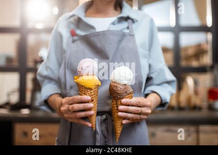 Verkäuferin hält zwei leckere Eiscreme im Waffelkegel im Laden, Nahaufnahme Stockfoto