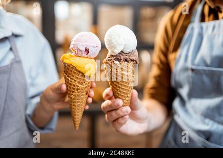 Zwei Verkäufer jubeln mit leckeren Eiscreme im Waffelkegel, haben Spaß beim Verkauf von Eis im Laden, Nahaufnahme Stockfoto