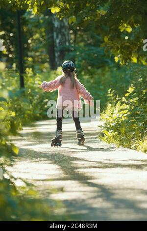 Ein Mädchen in rosa Pullover Skaten im Wald auf ihren Rollen. Mittlerer Schuss Stockfoto