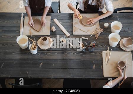 Draufsicht auf weibliche Töpfer während des Arbeitsprozesses in der Tonwerkstatt. Frau Meister bereiten Keramik-und Ton-Produkte an großen Holztisch Stockfoto