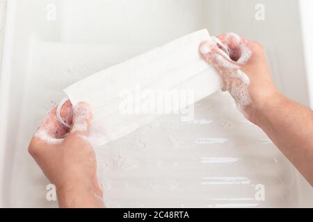 Frauenhände waschen eine wiederverwendbare Tuch Gesichtsmaske mit Seife In einem weißen Porzellanwaschbecken Stockfoto