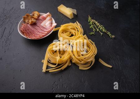 Zutaten aus Pasta Fettuccine mit Pilzen, Speck und Parmesan-Käse. Rohkost auf dunklem Graphit-Hintergrund mit Kopierfläche Stockfoto